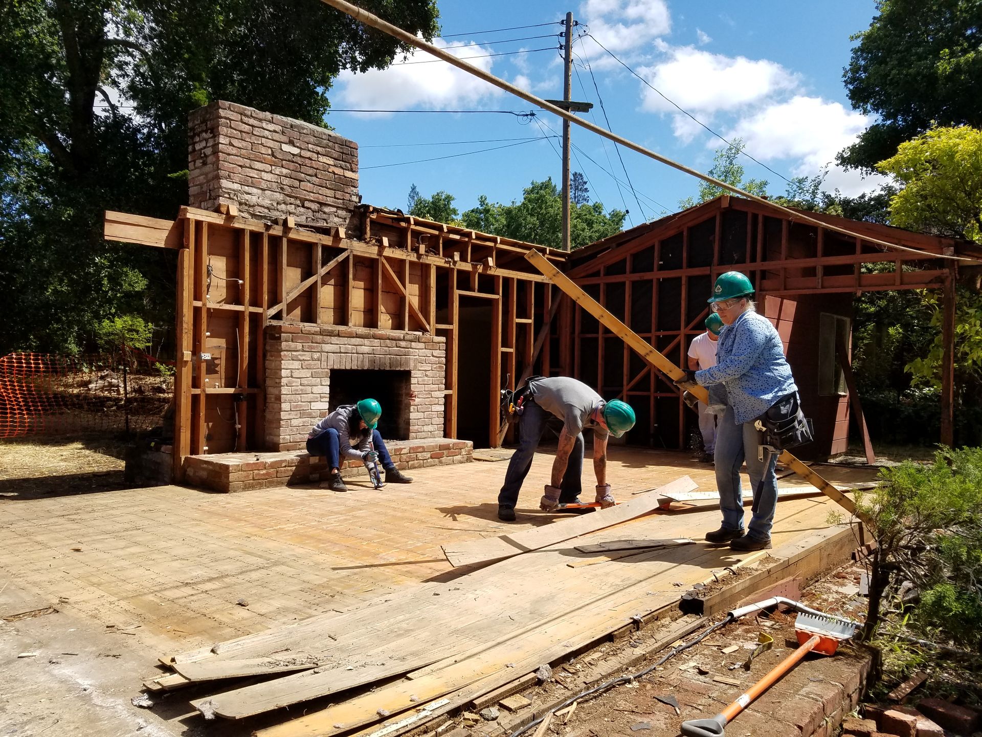 Construction zone with three people taking apart usable materials like wood panels.