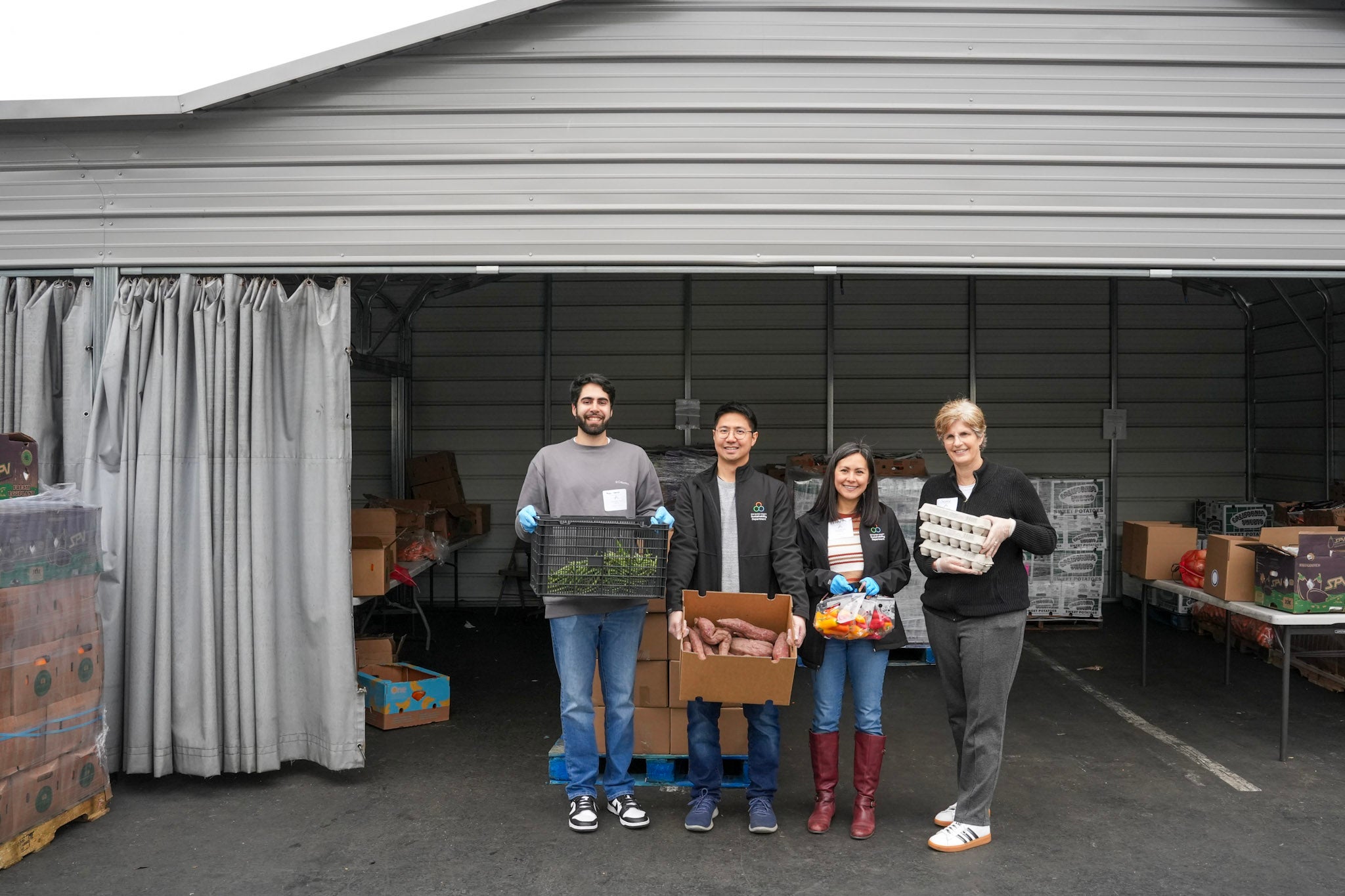 Four people holding boxes of fresh food in front of a warehouse